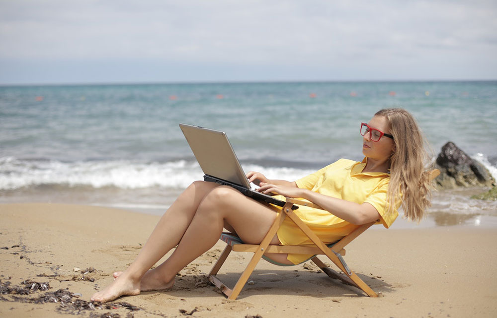 Girl on beach working on her laptop as a digital nomad
