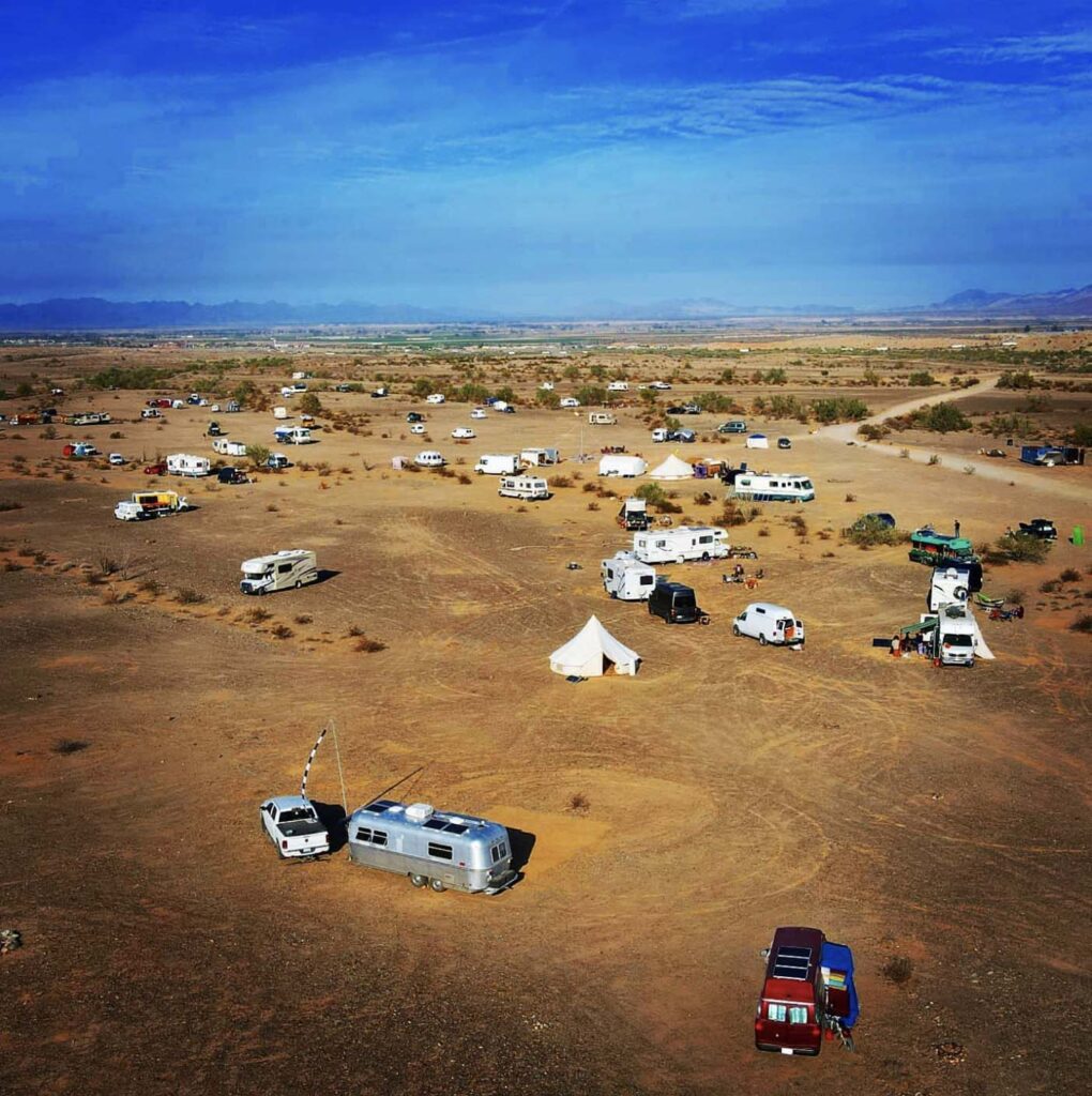 A group of vehicle dwellers, vanlifers, and digital nomads camping together in the desert during a large nomad gathering.